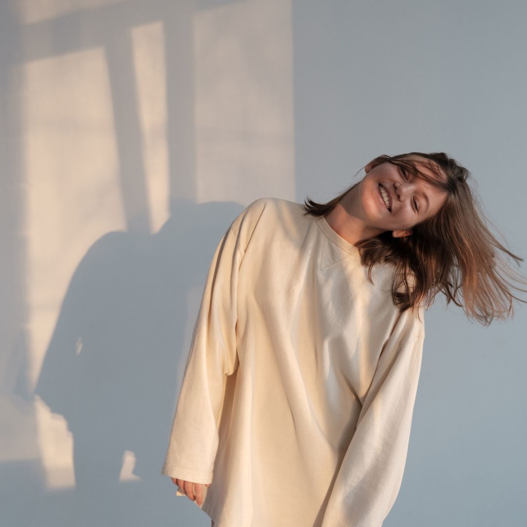 girl in front of a window, wearing a sweater turning her head and hair down