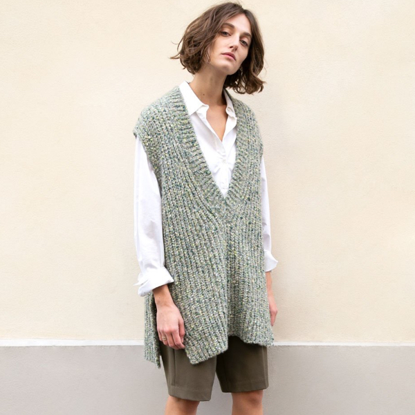 Model in front of a beige wall wearing an oversized vest top paired with white shirt and bermuda by The Frankie Shop