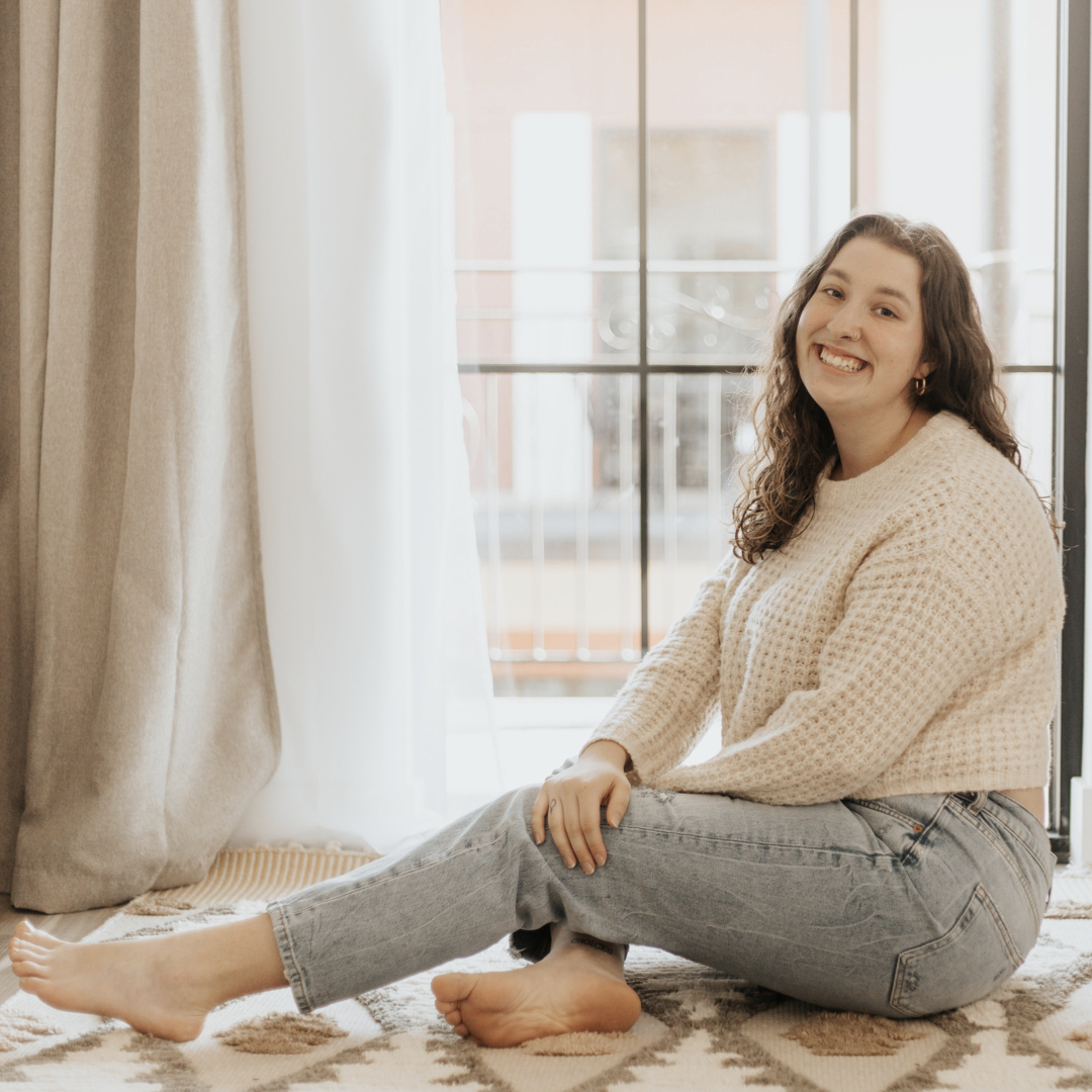 Plus size woman sitting by the window smiling.