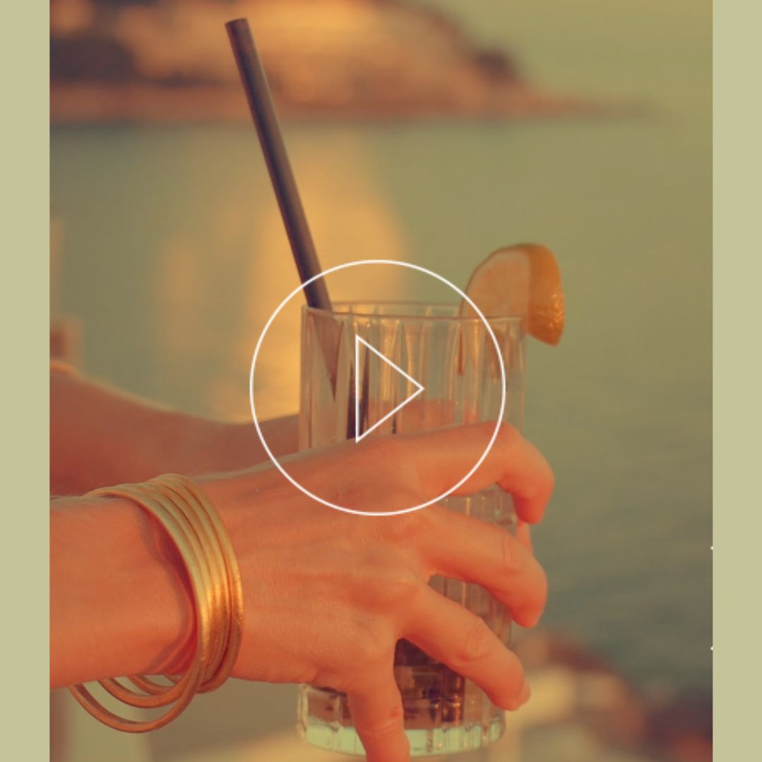 detail of a female hand holding a glass of a juice against a maritime scenery