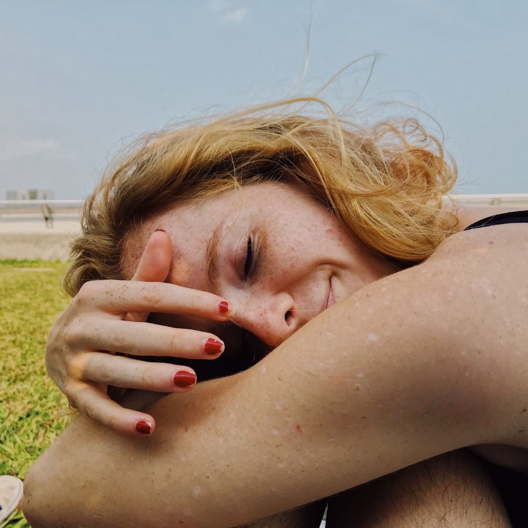 close up fo a ginger woman with the eyes closed and with the hands around her knees on a beach