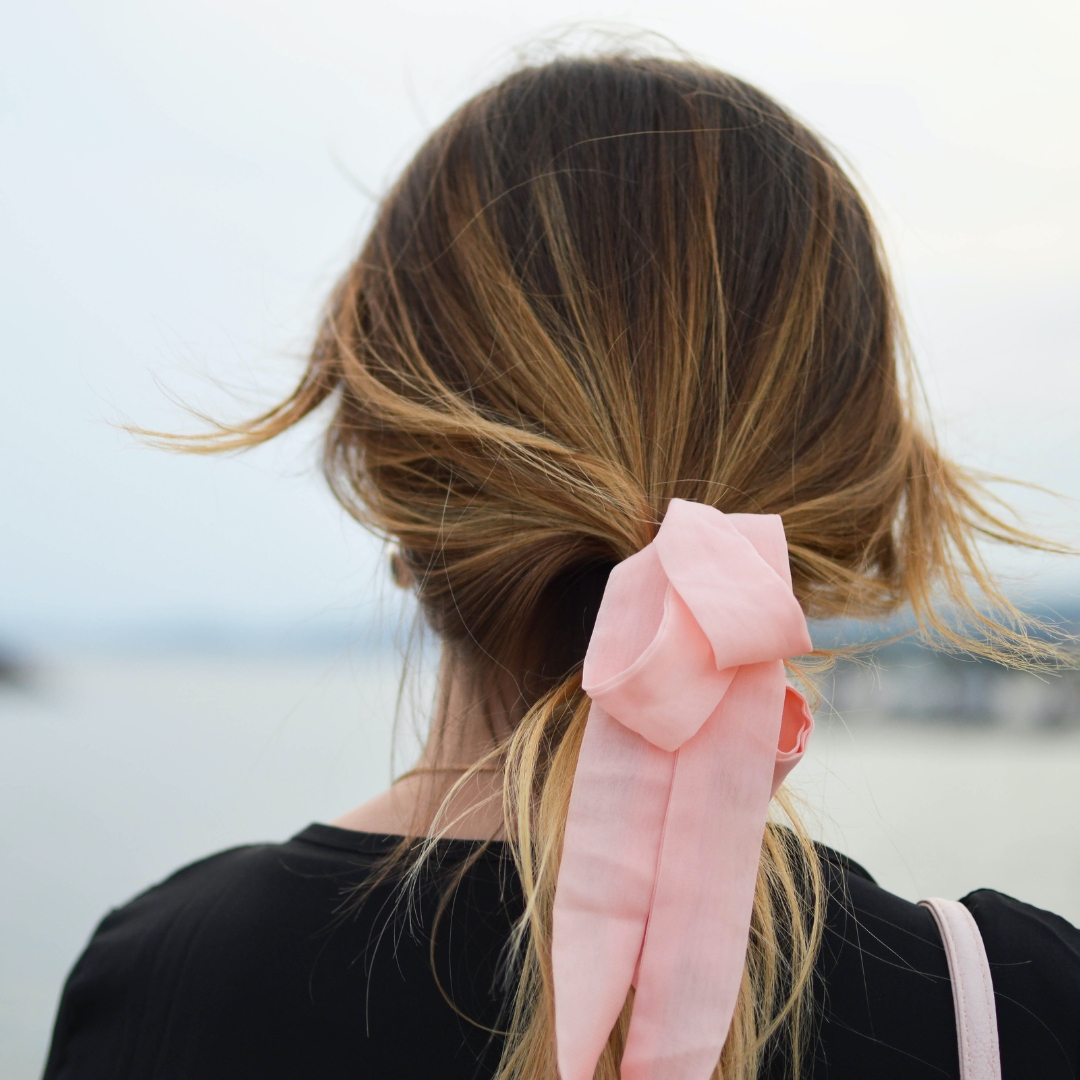 Detail of a woman wearing a ponytail with a pink bow showing a healthy hair