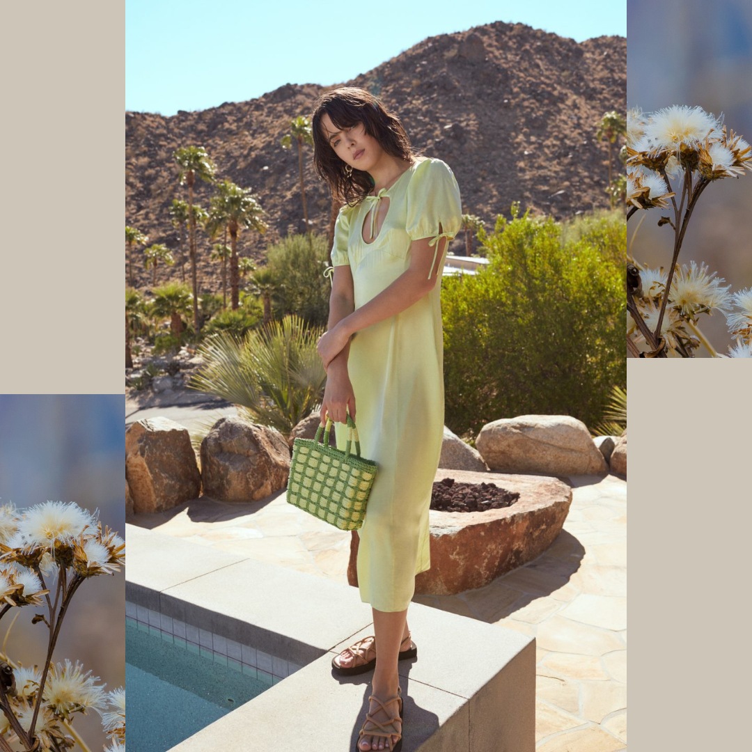 model wearing a satin lime dress stands in a garden with a swimming pool