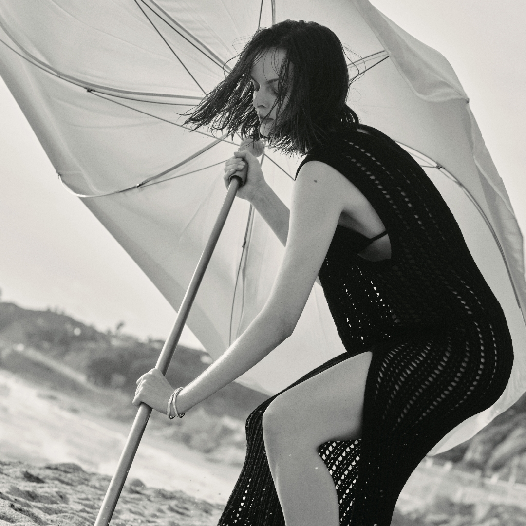 model opens a sun umbrella on the beach and she is wearing a black crochet dress cover