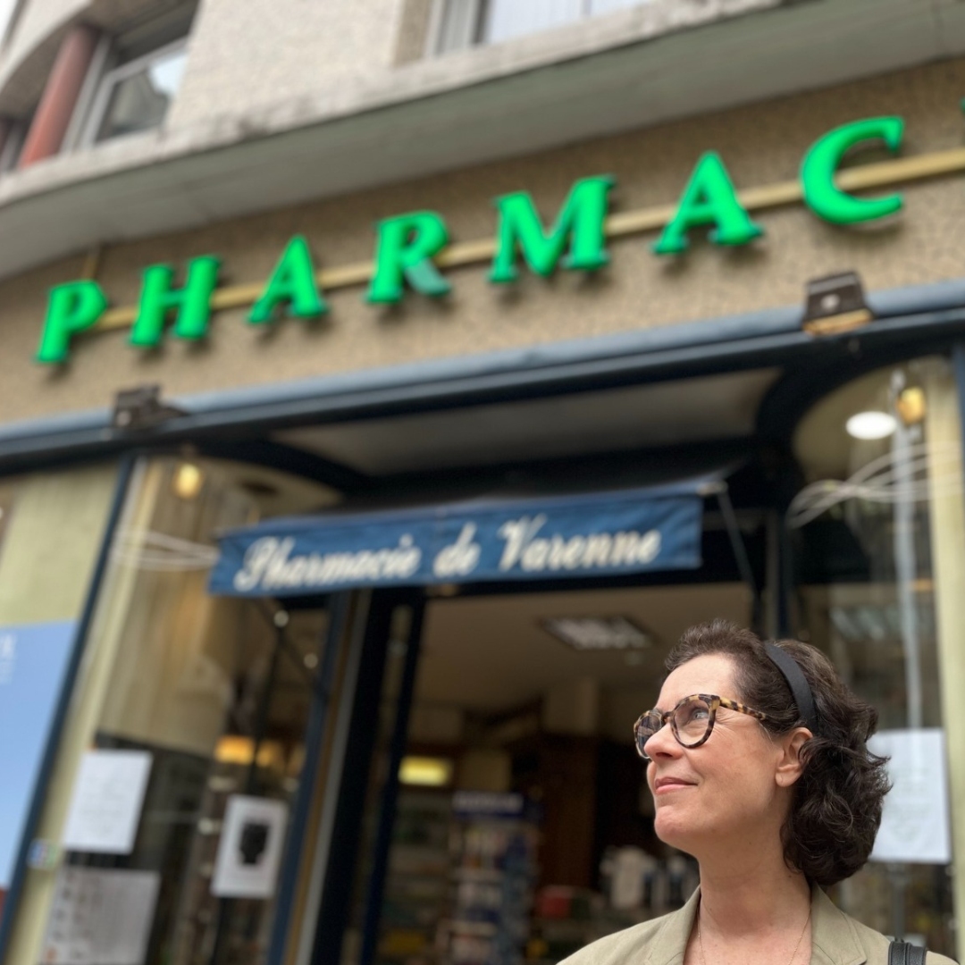 notorious editor in chief standing in front of a French Pharmacie