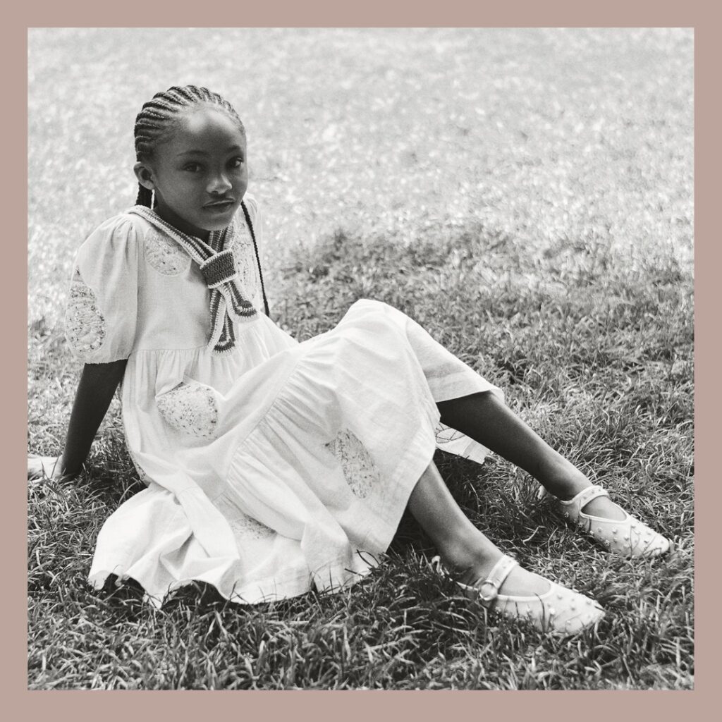 a little black girl id sitting on a grass in a park wearing a embroidered white dress from Zara and Sea Children Collection