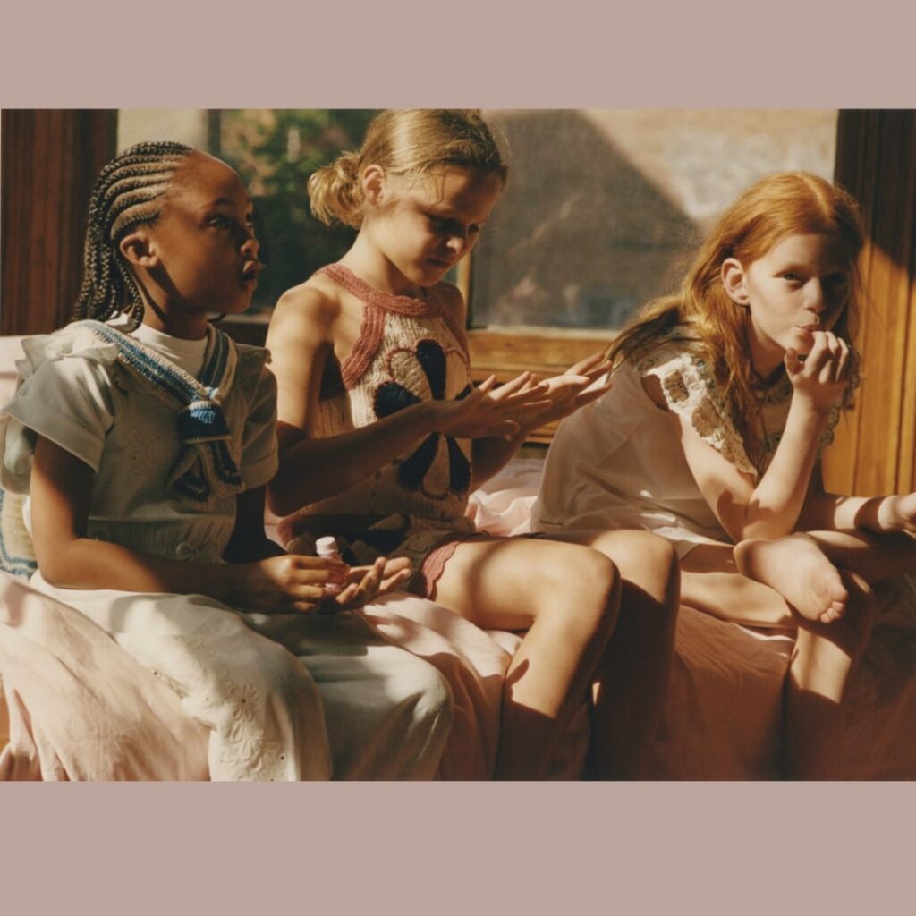 three girl are sitting on a bed in a sunny bedroom, having fun together and they all are wearing dresses from Zara and Sea Children Collection