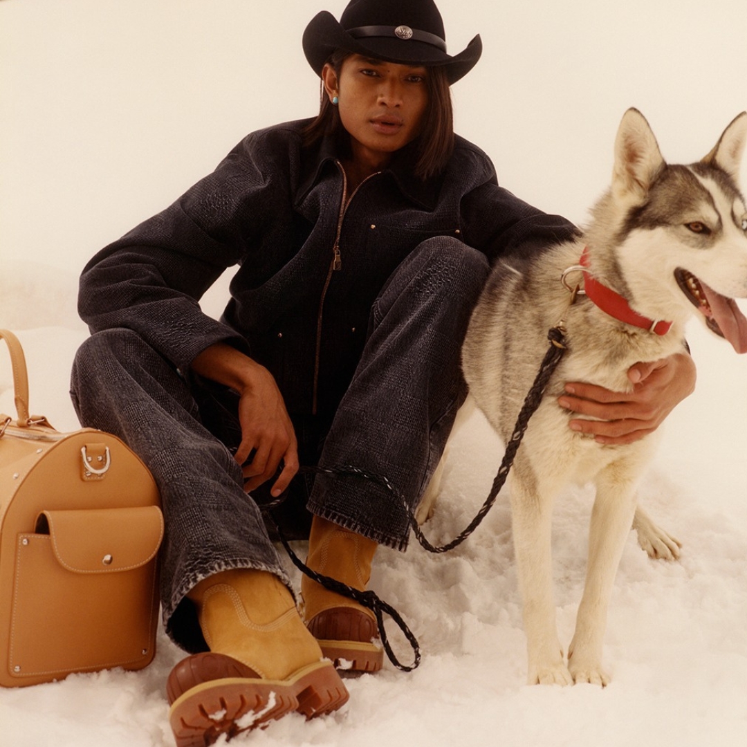 Louis Vuitton male model is sitting on a snow embracing a dog. He is wearing aw24 western inspired collection