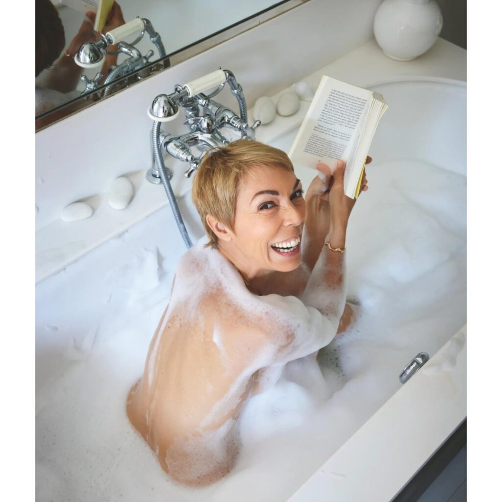 Mathilde Favier in the bathtube, reading her book about Paris, looks at the camera and smiles