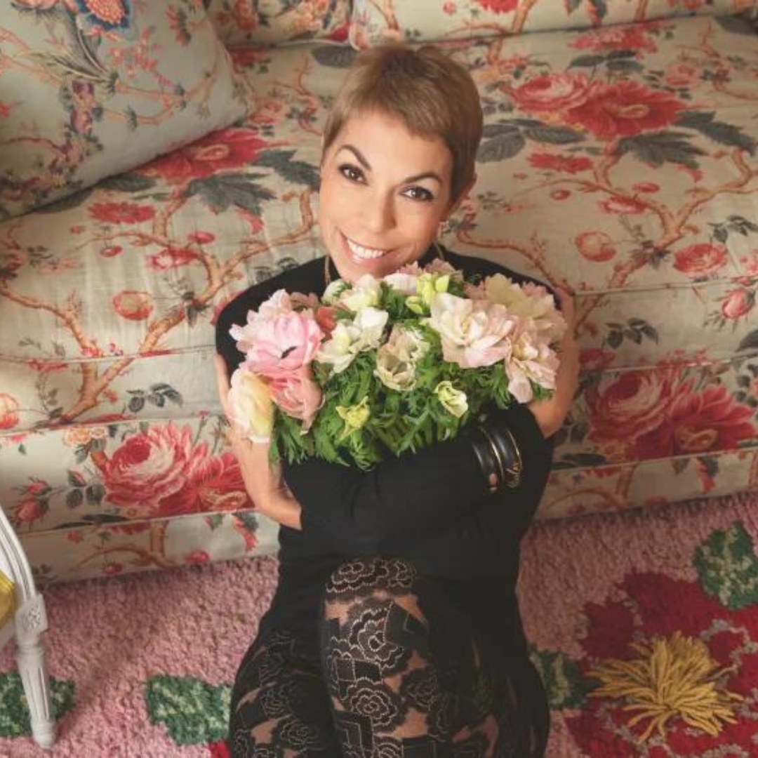 Mathilde Favier holding a flower bouquet while sitting on a floral hug in front a floral sofa