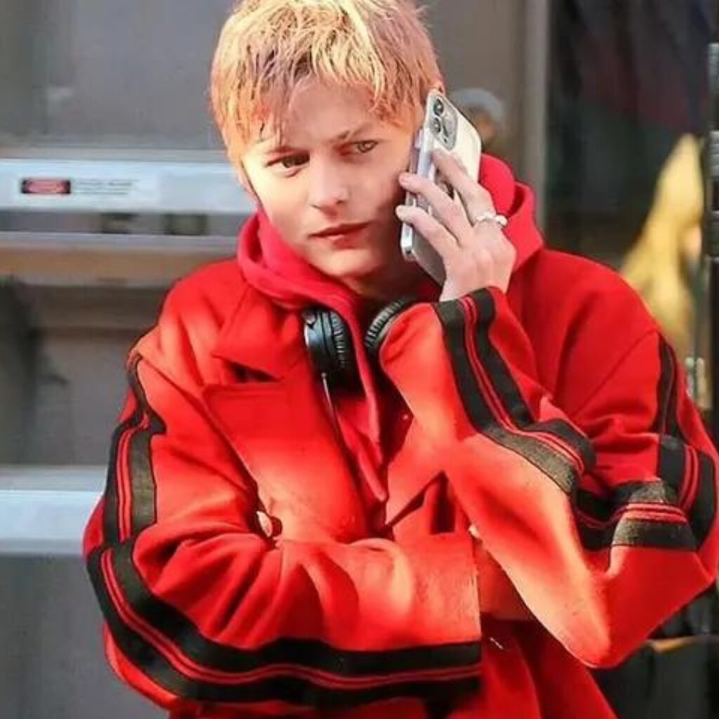 Emma Corrins wearing an iconic red jacket in A Murder at The End of The World and rocking a Oasis haircut