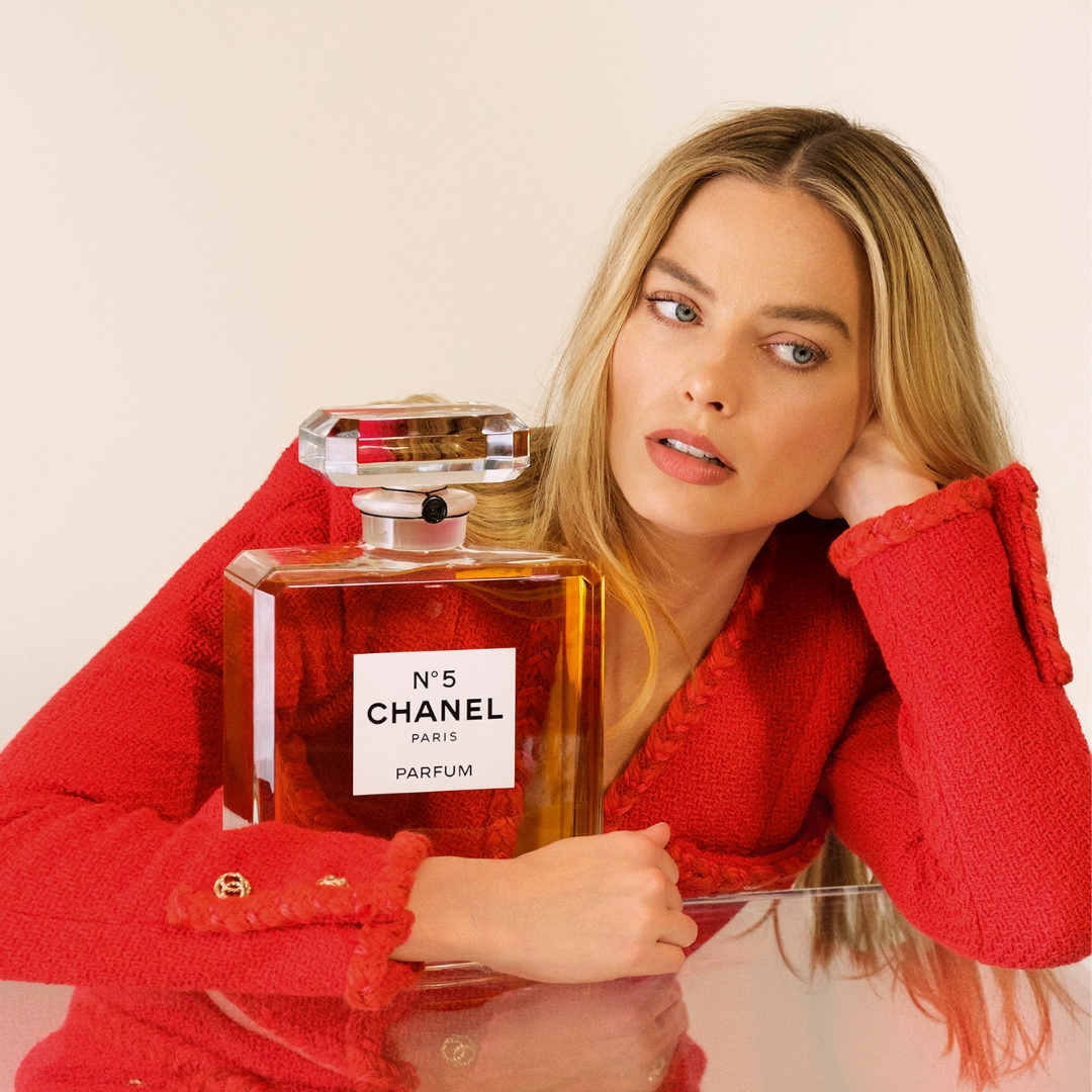 Actress Margot Robbie wearing a Red Jacket embrace a extra big bottle of CHanel N5 eau de parfum