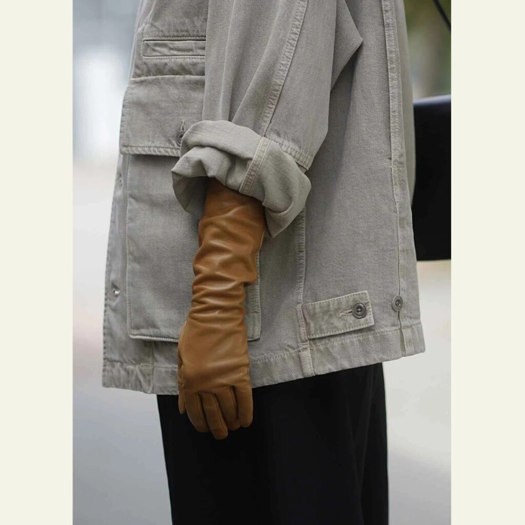 detail of a woman wearing a caramel long glove paired with a oversized denim jacket and black pants - Handsome Stockholm