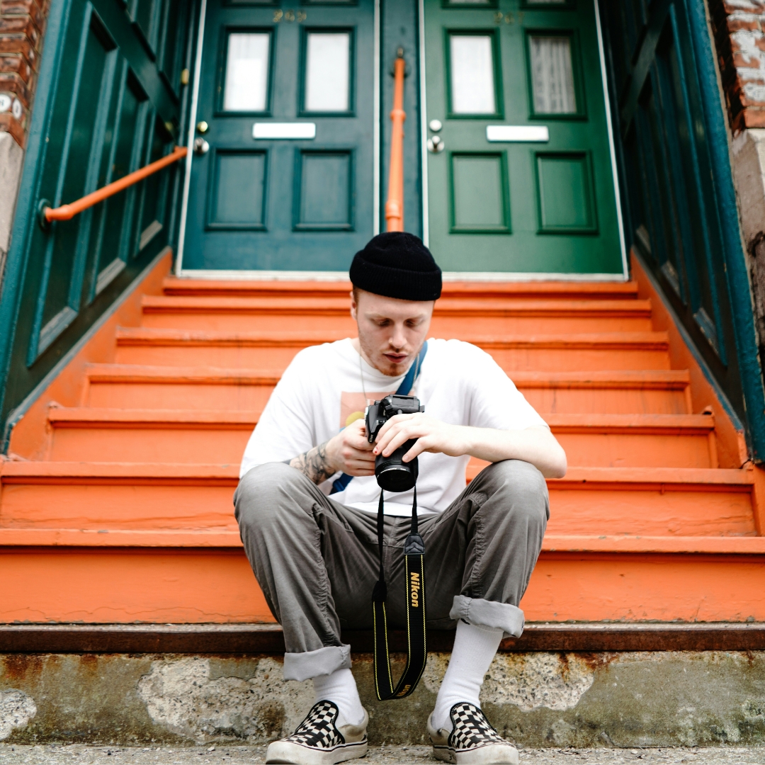 young man sitting on the front stair of his house while he checks some photos in his photocamera