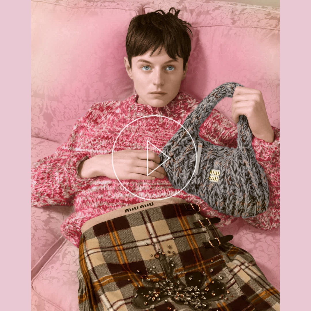 Emma Corrin on a pink sofa wearing pullover, bag and a plaid skirt from the Miu Miu upcycled collection for a sustainable Christmas