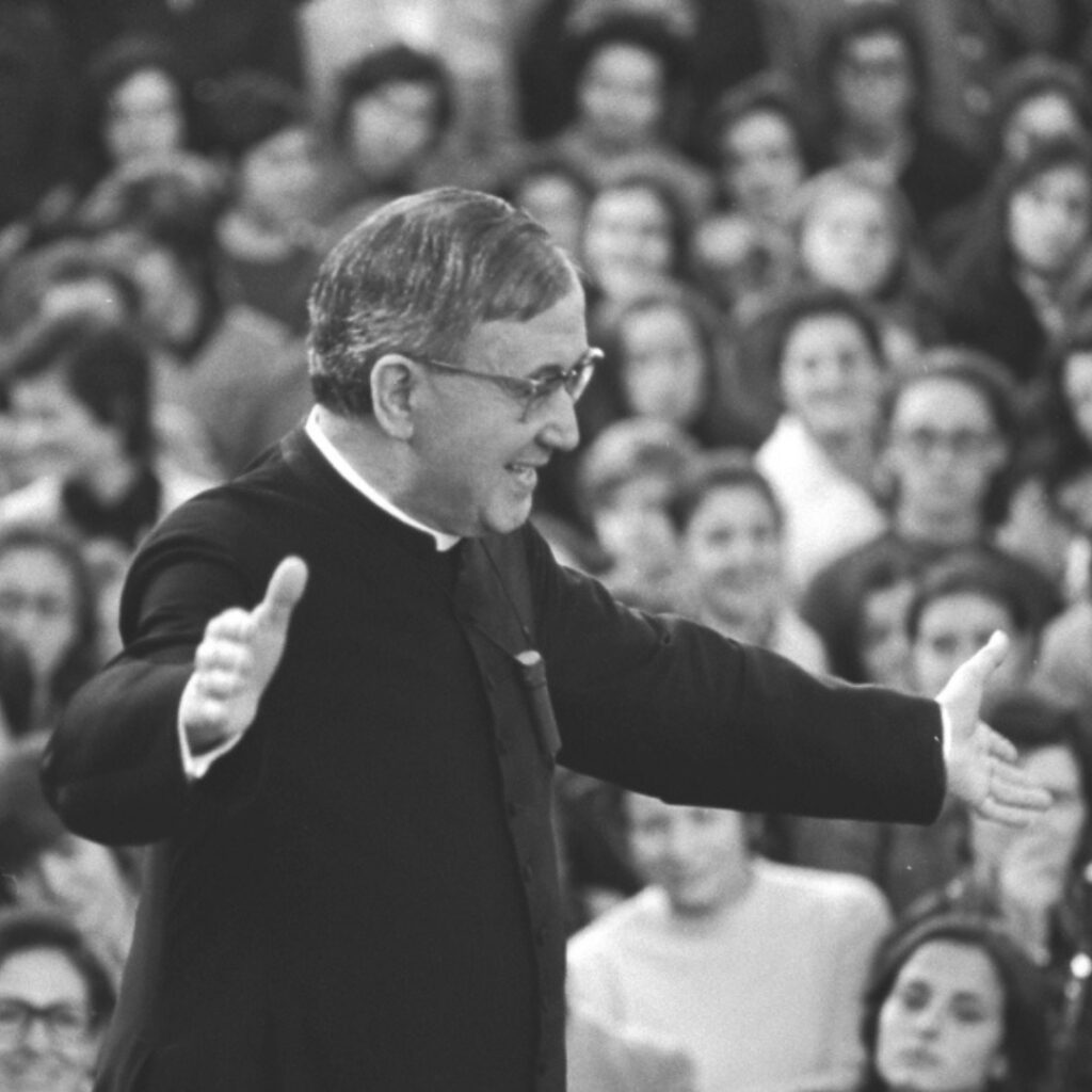 black and white image of Saint Josemaria with open arms talking to an audience of catholics