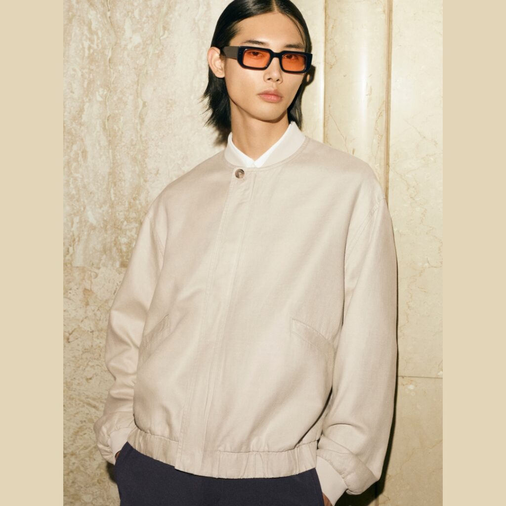 model wearing a slim beige bomber jacket paired with orange lens sunglasses-COS SS25 collection