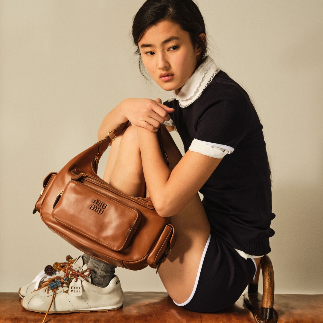 Miu Miu model sitting on a gymnastic leather bar wearing a retro sneaker