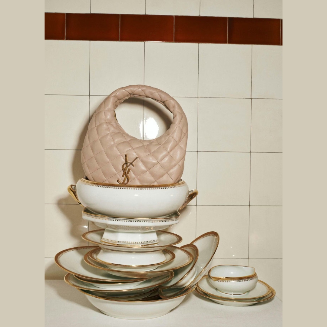 still life showing a Saint Laurent bag on top of a pile of vintage dinner table set