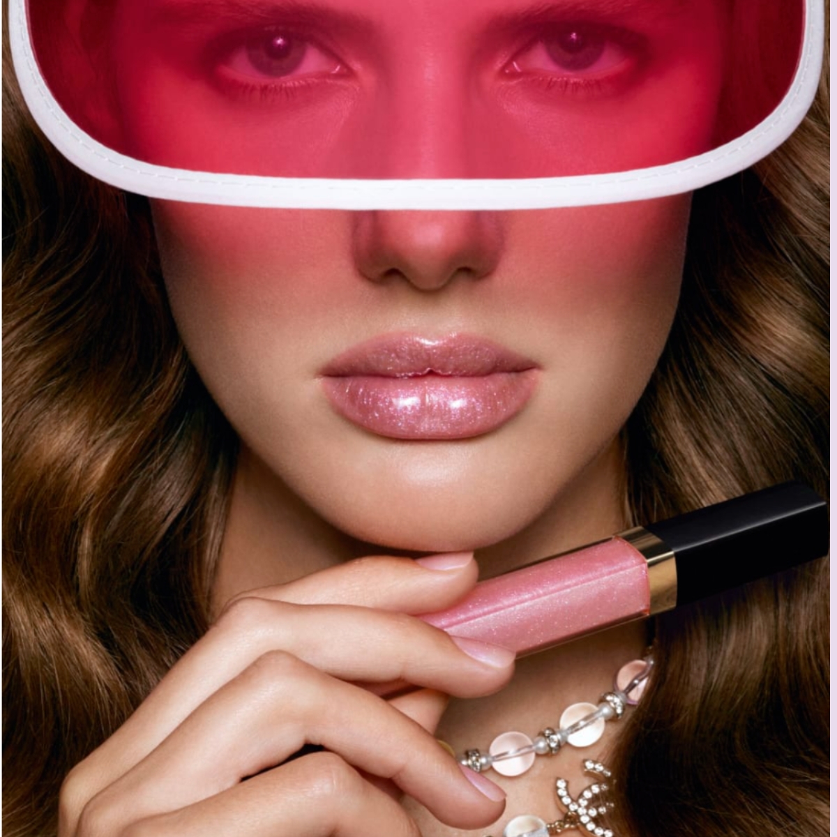 model wearing a pink visor holding in front of the camera a lipgloss from chanel