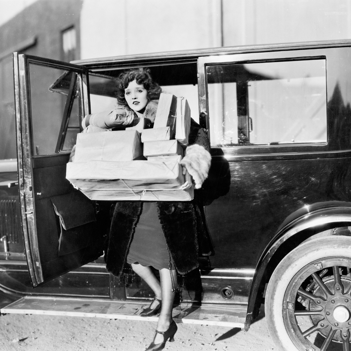 vintage black and white photo with a woman coming down from a car carrying many gift packages